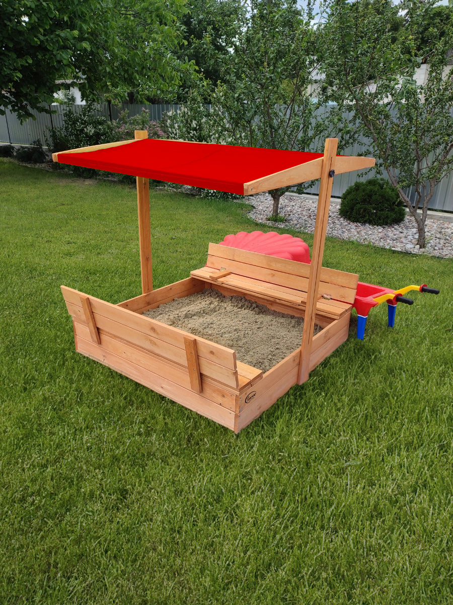 Houten zandbak met bank, rood dakje, open zandbak met bankjes in een groene tuin, ideaal voor kinderen.