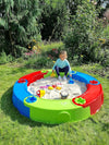 Kleurrijke ronde plastic zandbak buiten met worteldoek, een kind speelt in het zand in de tuin. Perfect voor buitenspel.