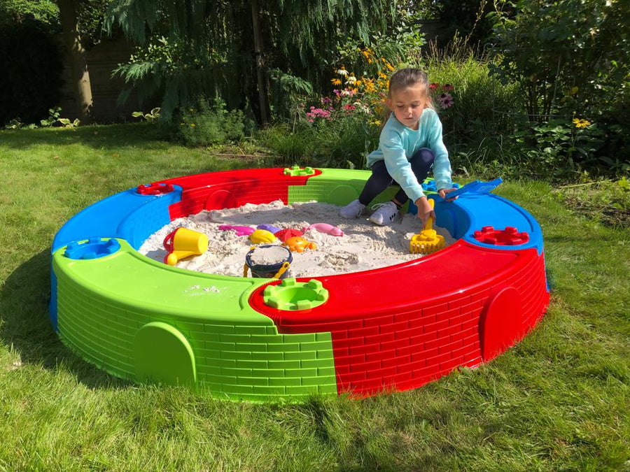 Kleurrijke ronde plastic zandbak buiten met worteldoek, een kind speelt in het zand in de tuin. Perfect voor buitenspel.